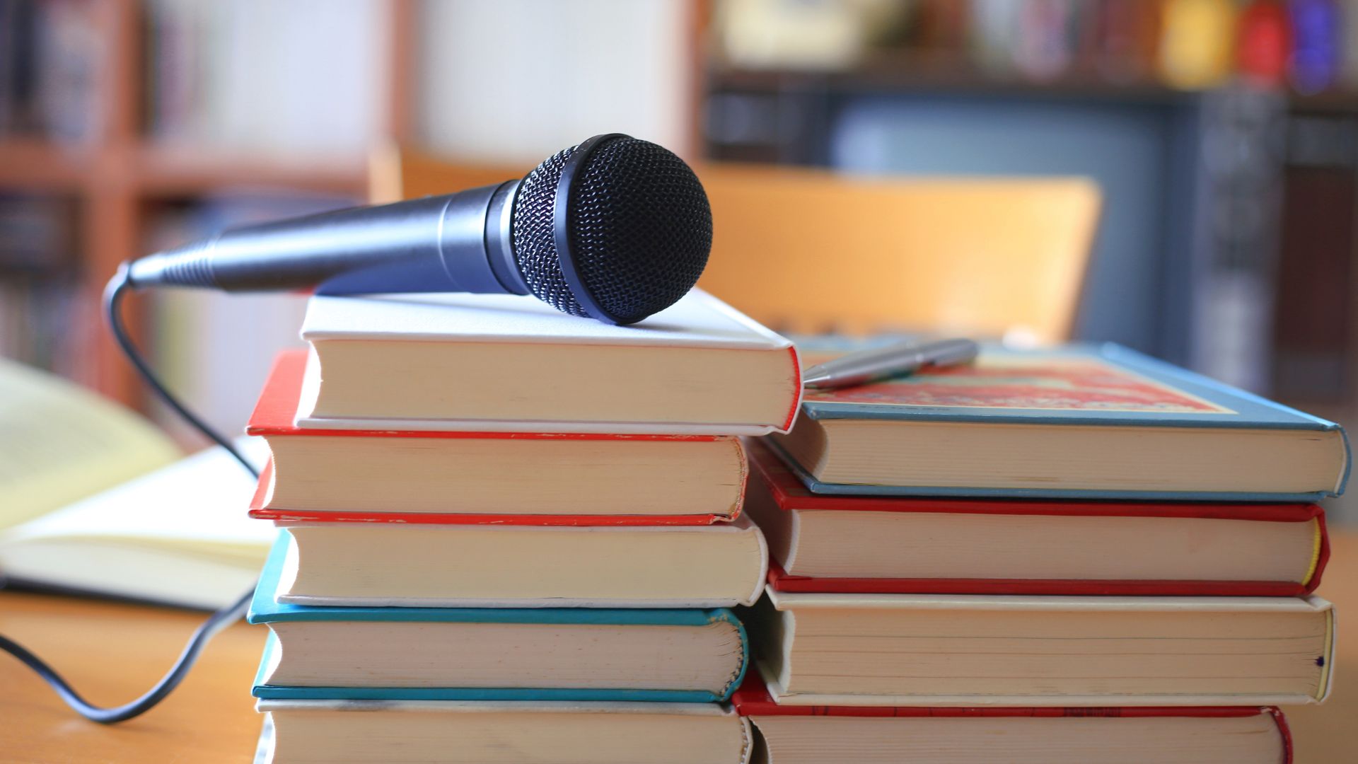 Author Talks and Readings events photo. Nine books are sitting on a table or desk and there is a corded microphone sitting on top of some of the books.