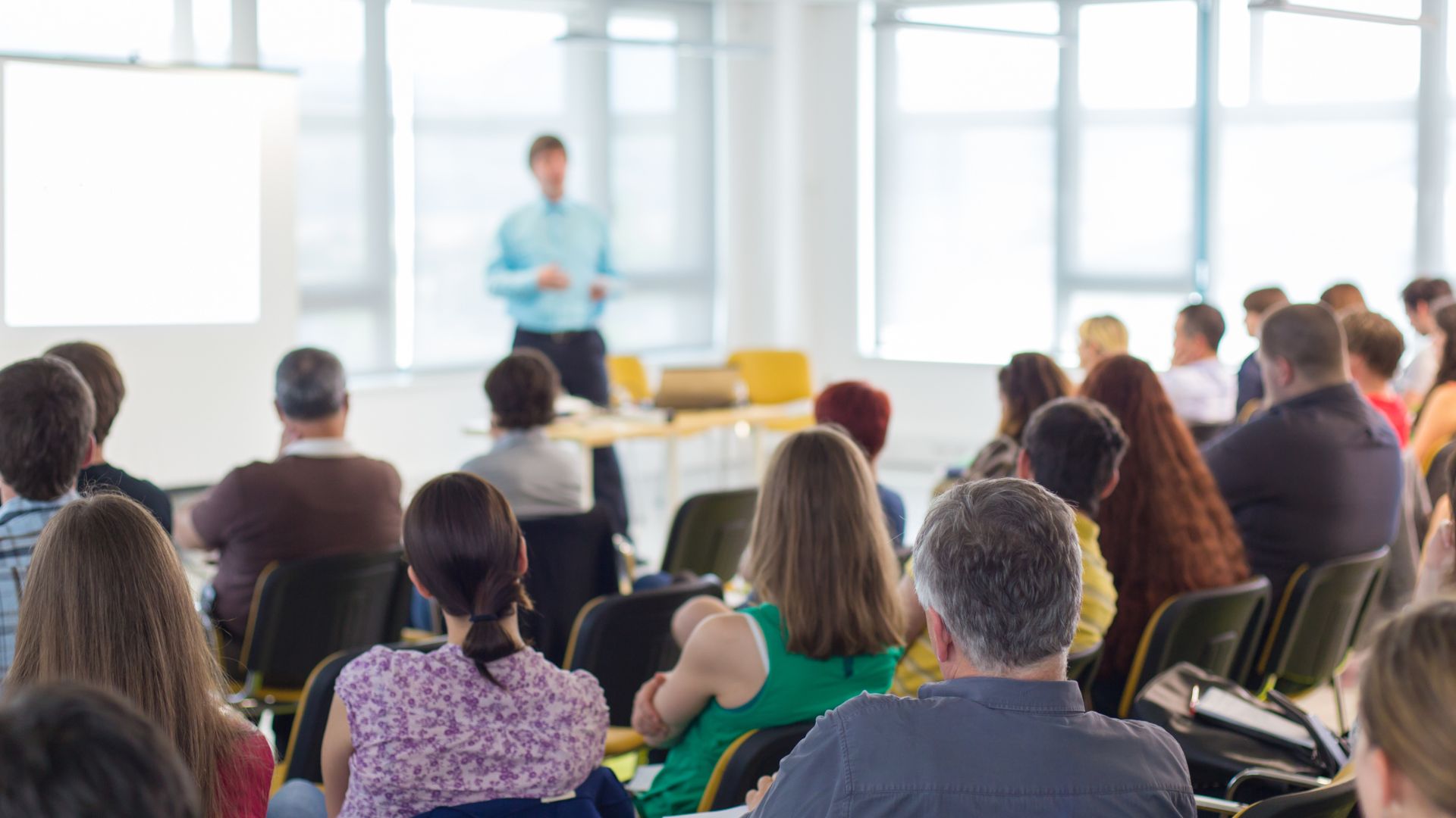 Information Sessions events photo. An speaker stands at the front of a room facing an audience of people sitting in front of them.